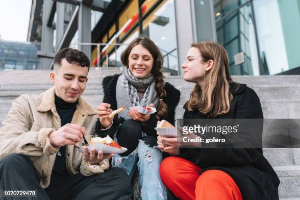 three young travellers having curry sausage outdoors in berlin - currywurst stock pictures, royalty-free photos & images