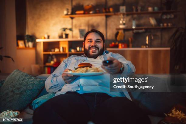 übergewichtiger mann essen fast food und vor dem fernseher - schlechte angewohnheit stock-fotos und bilder