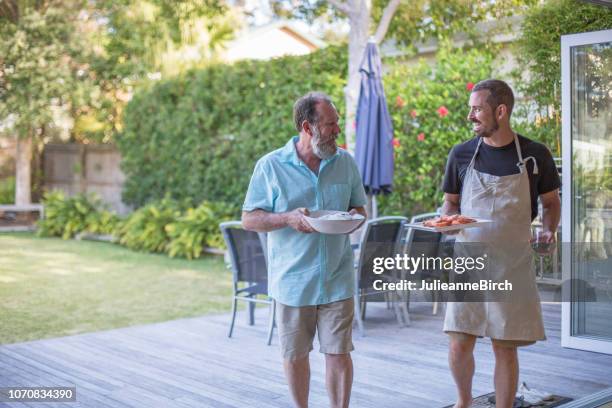 vader en zoon lopen binnenshuis met gebarbecued voedsel praten - australian bbq stockfoto's en -beelden