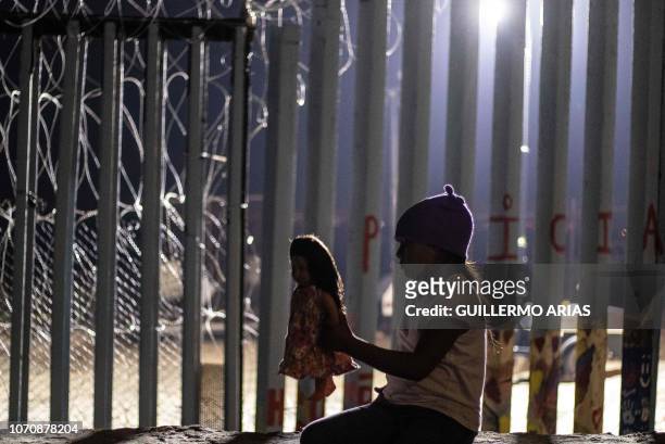 Girl from Guatemala, part of the Central American migrant caravan, plays with a doll near the US-Mexico border fence in Playas de Tijuana, Baja...