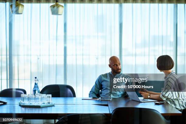 female manager talking to male colleague in board room - disturbios fotografías e imágenes de stock