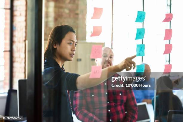 young businessman pointing to sticky note on window - thinking outside the box englische redewendung stock-fotos und bilder