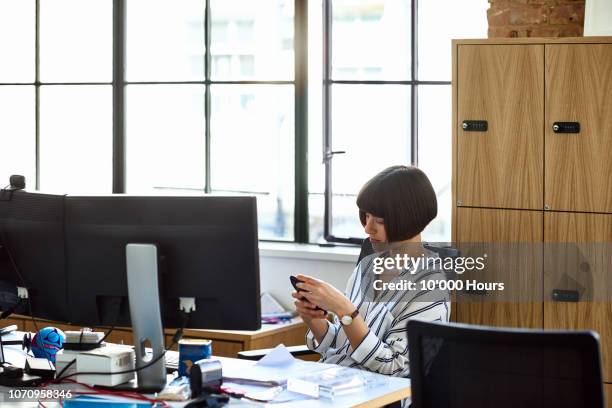 attractive businesswoman at desk using mobile phone - procrastination stock-fotos und bilder