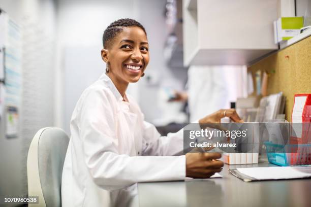 sonriendo químico trabajando en escritorio - pharmacist fotografías e imágenes de stock