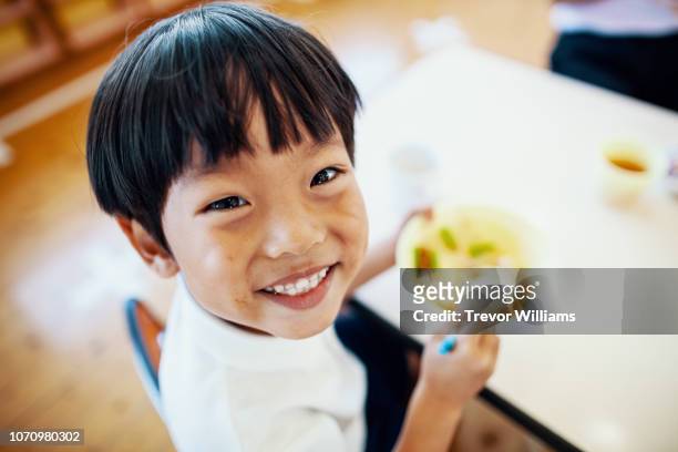 young boy eating his school lunch at preschool - asian young boy smiling stock pictures, royalty-free photos & images
