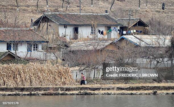 North Korean woman carries buckets for water outside decrepit homes amid the dry and barren landscape on the banks of the Yalu River, some 70 kms...