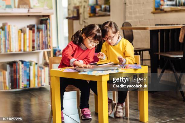 Two sisters with Down syndrome sitting at the table in kindergarten