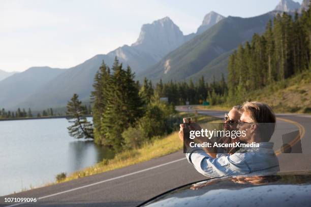 couple pause à côté de la voiture, prendre la photo sur la route de montagne - car top view photos et images de collection