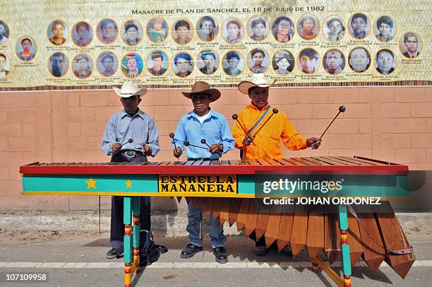 Indigenous musicians play the marimba next to a perimeter wall with the pictures of victims of the Guatemalan armed conflict , during its...