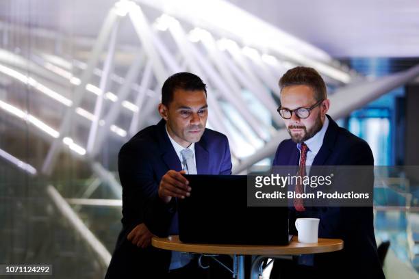 two businessmen looking at a laptop in waiting area - financieel beroep stockfoto's en -beelden