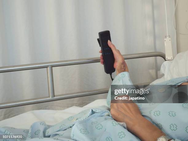 sick woman in a hospital raising the electric bed with the remote control - iv drip womans hand stock-fotos und bilder