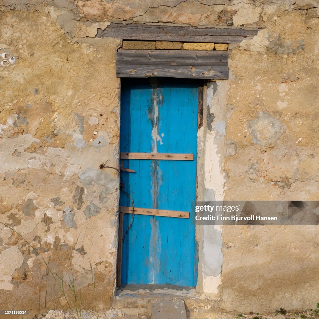 Old blue door in a grungy concrete wall. Old barn in Sicily