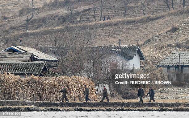 North Korean men walk amid a dry and barren landscape on the banks of the Yalu River some 70 kms north of Dandong in northeast China's Liaoning...