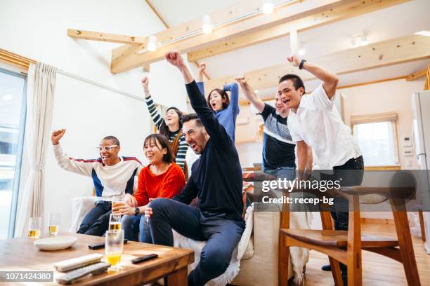 group of multi-ethnic friends watching tv with beer and pizza at home party - cheering encouragement stock pictures, royalty-free photos & images