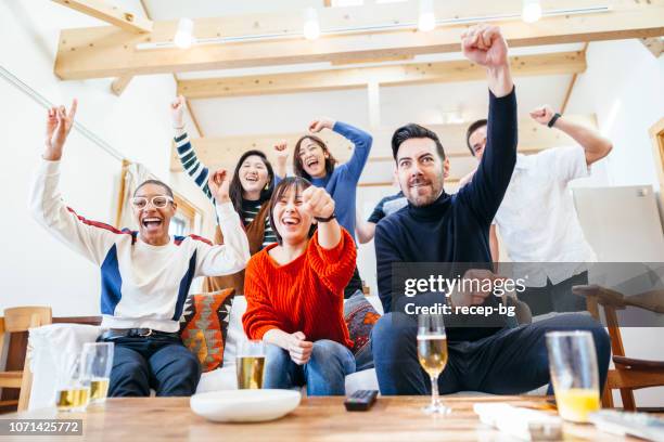 group of multi-ethnic friends watching tv with beer and pizza at home party - cheering encouragement stock pictures, royalty-free photos & images