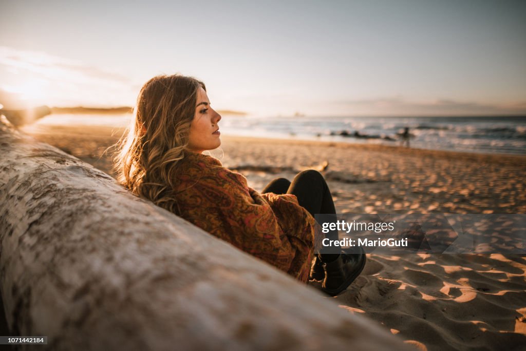 Young woman sitting by a beach at sunset in winter