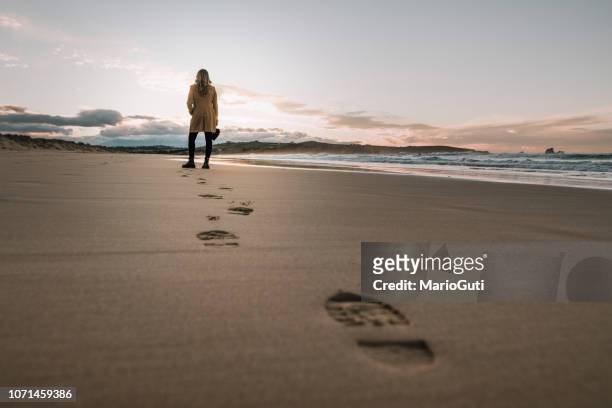 young woman walking over a beach and leaving her footprints on the sand - footprint stock pictures, royalty-free photos & images