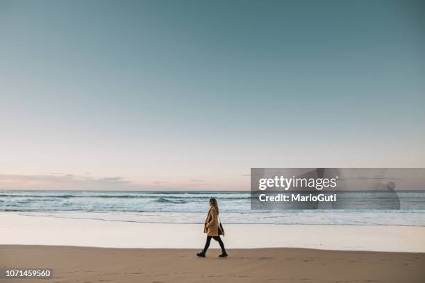 seitenansicht der jungen frau zu fuß am strand bei sonnenuntergang - winter strand stock-fotos und bilder