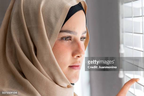 concerned muslim young woman looking through a window - tunisian islamist stock pictures, royalty-free photos & images