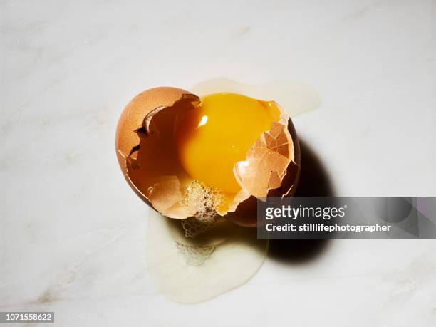 broken egg in shell on white marble background - cracked egg stock-fotos und bilder