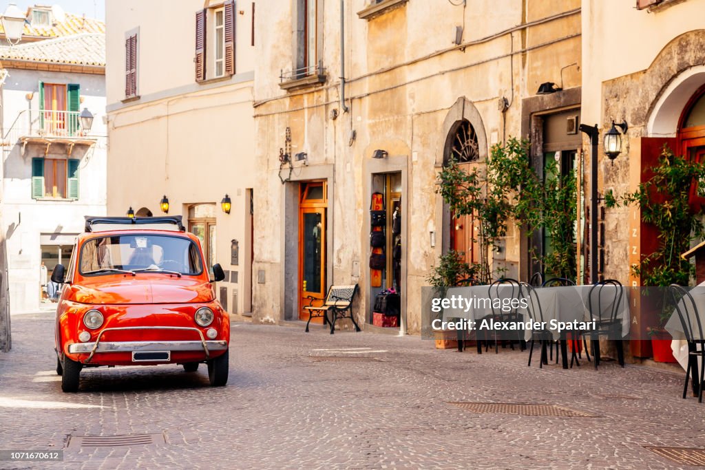 Old red small vintage car on the street of Italian city on a sunny day