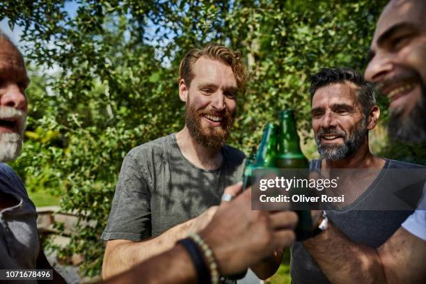 cheerful friends clinking beer bottles in garden - man sipping beer smiling stockfoto's en -beelden