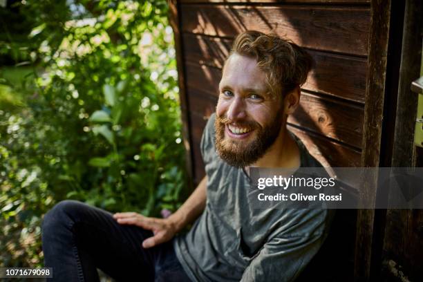 portrait of smiling bearded man resting at garden shed - pelo facial imagens e fotografias de stock