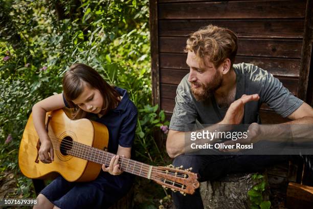 father and daughter sitting at garden shed playing guitar - playing music together stock-fotos und bilder