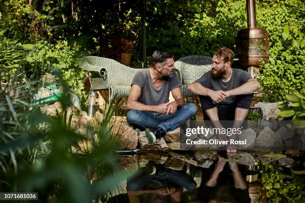 two men sitting together at garden pond talking - facial hair stock pictures, royalty-free photos & images