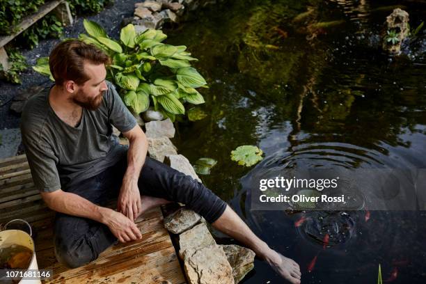 man sitting together at garden pond with foot in water - teich stock-fotos und bilder