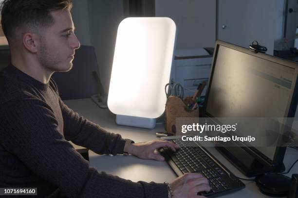 young man working at the office with light therapy lamp - winterdepression stock-fotos und bilder