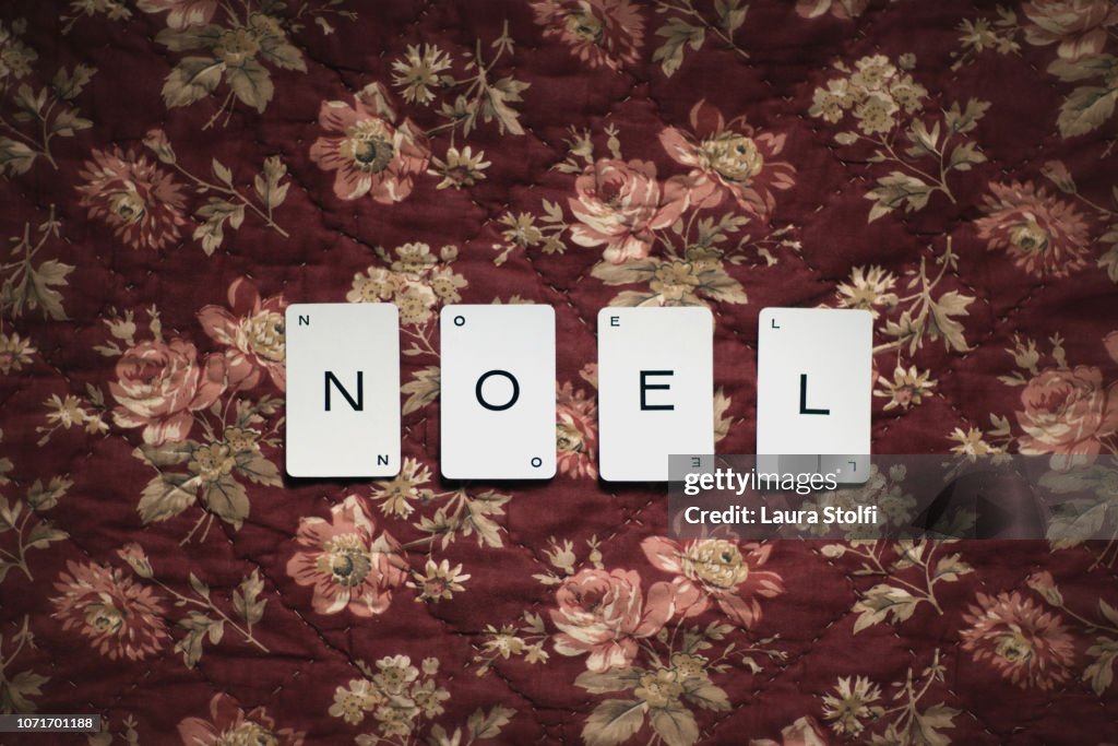 Card game cards spelling the word Noel (Christmas in french language) over flowered bordeaux quilt