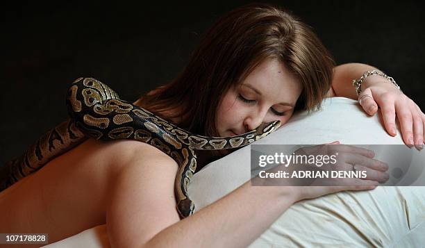 Carly, an employee at Chessington World of Adventures, poses for pictures as she enjoys a massage by two Royal Python snakes at a photocall to...