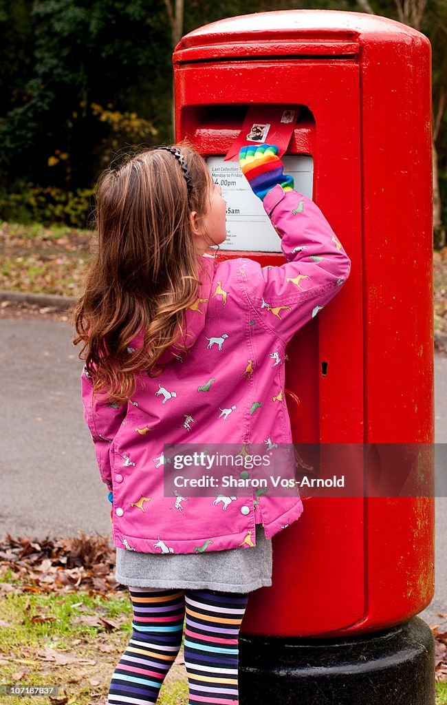Young girl posting a letter into a red letterbox