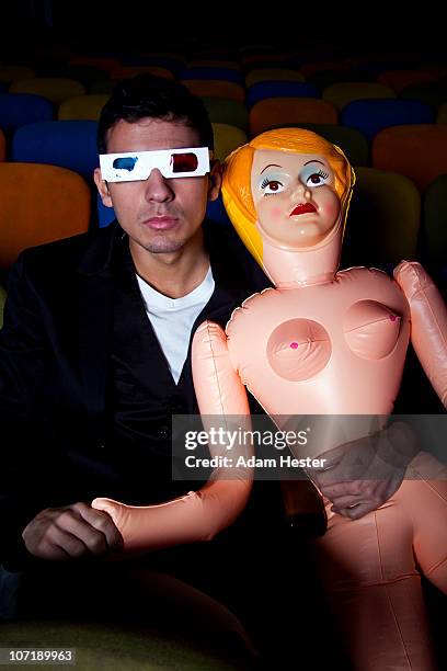 a young man holding a blow up doll in a theater. - mann gummipuppe stock-fotos und bilder