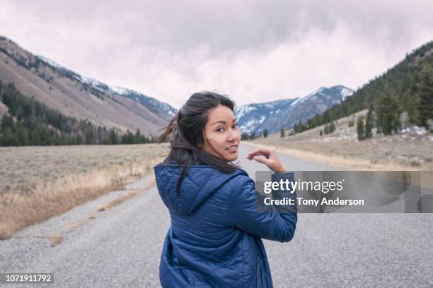 young woman walking on mountain road on cold cloudy day - portrait looking over shoulder stock pictures, royalty-free photos & images