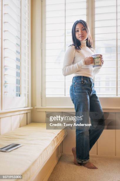 young woman inside home wearing sweater drinking from a mug - hot vietnamese women stock pictures, royalty-free photos & images