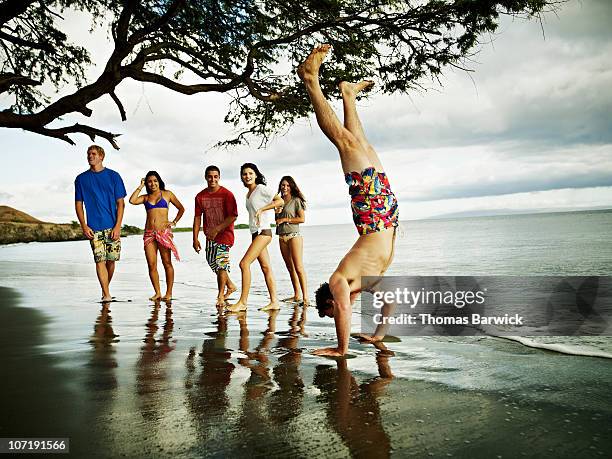 group of teens watching friend do handstand - muscle men at beach stock-fotos und bilder