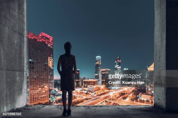 young female looking out over city at night - peking skyline stock-fotos und bilder