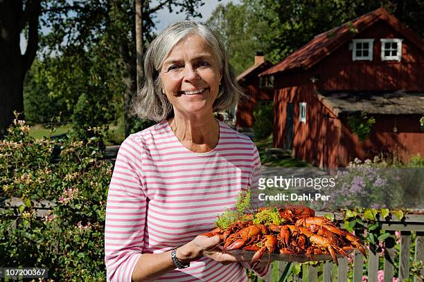senior woman holding plate of cray fish in garden - crayfish stock pictures, royalty-free photos & images