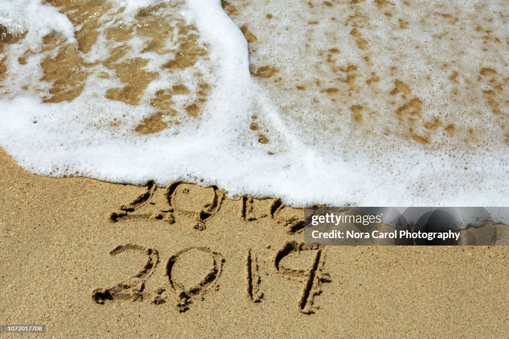 New Year 2019 and Year 2018 Written on Sandy Beach with Waves