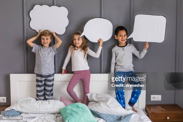 happy kids with speech bubbles on a bed in bedroom. - kids placard stock pictures, royalty-free photos & images