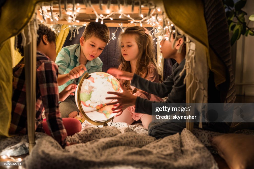 Group of small kids exploring globe in a tent at home.