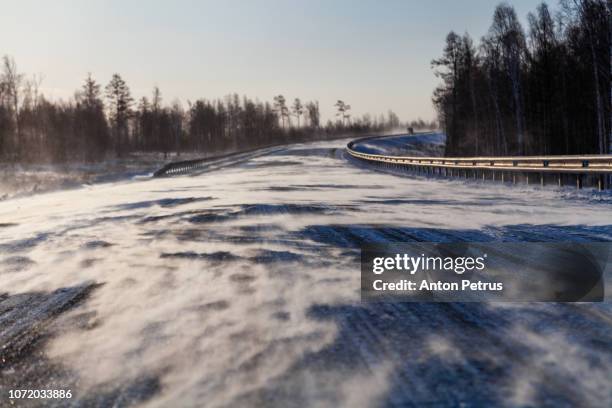 drifting snow on winter road with snowdrifts on the roadside in the snowstorm on a sunny day. - snow covered road stock-fotos und bilder