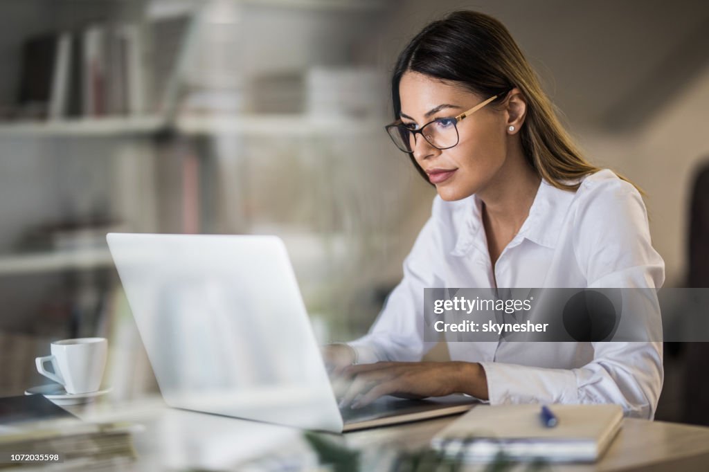 Giovane imprenditrice che digita un'e-mail su laptop all'ufficio di casa.