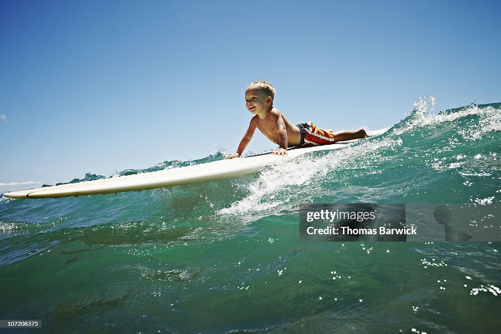 Toddler riding wave on surfboard smiling