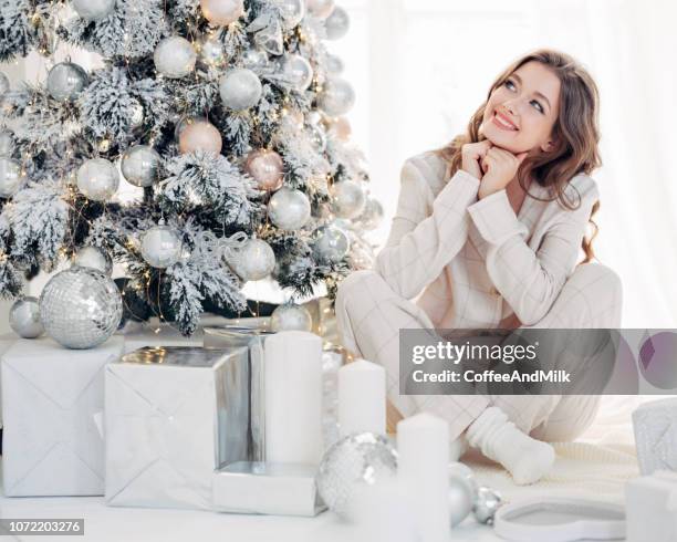 beautiful girl sitting in a cozy atmosphere near the christmas treea - christmas tree presents stock pictures, royalty-free photos & images