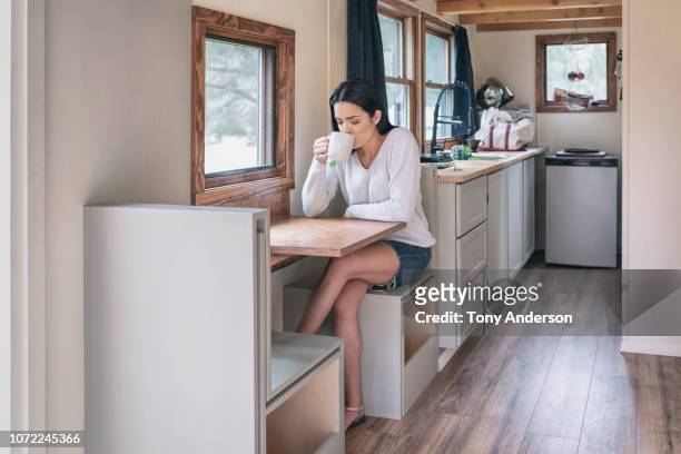 young woman having tea in her tiny house - wohngebäude innenansicht stock-fotos und bilder