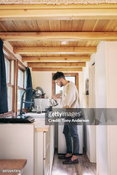 young man making coffee in kitchen of tiny house - wohngebäude innenansicht stock-fotos und bilder