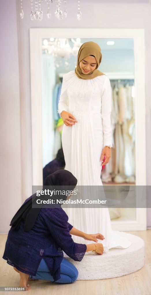 Alfaiate muçulmano feminino coloca toques na bainha do vestido de casamento